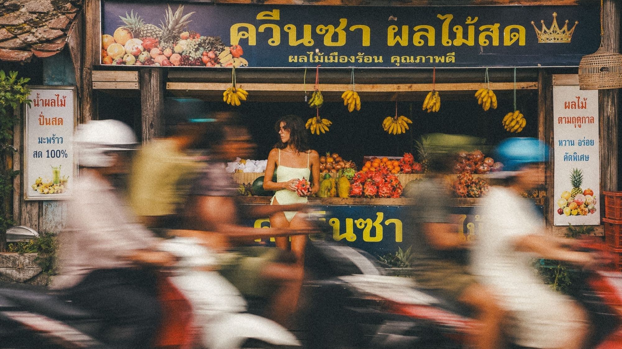 A fruit stall at the roadside, scooters blurring past